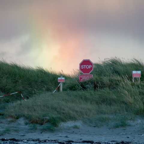 Stop signage at the airport beach on Benbecula, with a rainbox in the background.